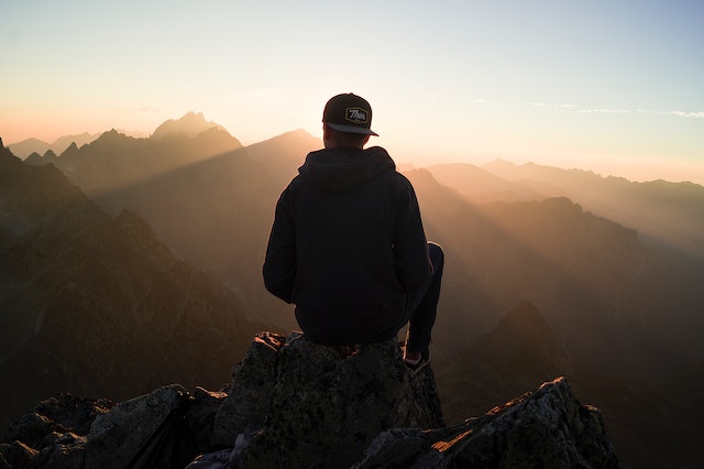 man sitting and looking at sunset mountains